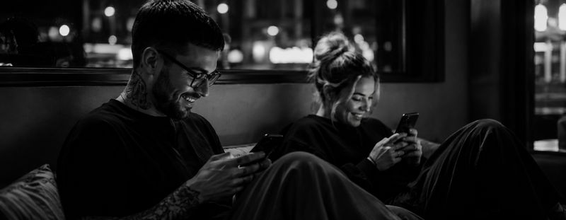 Two people laughing at their phones on a sofa